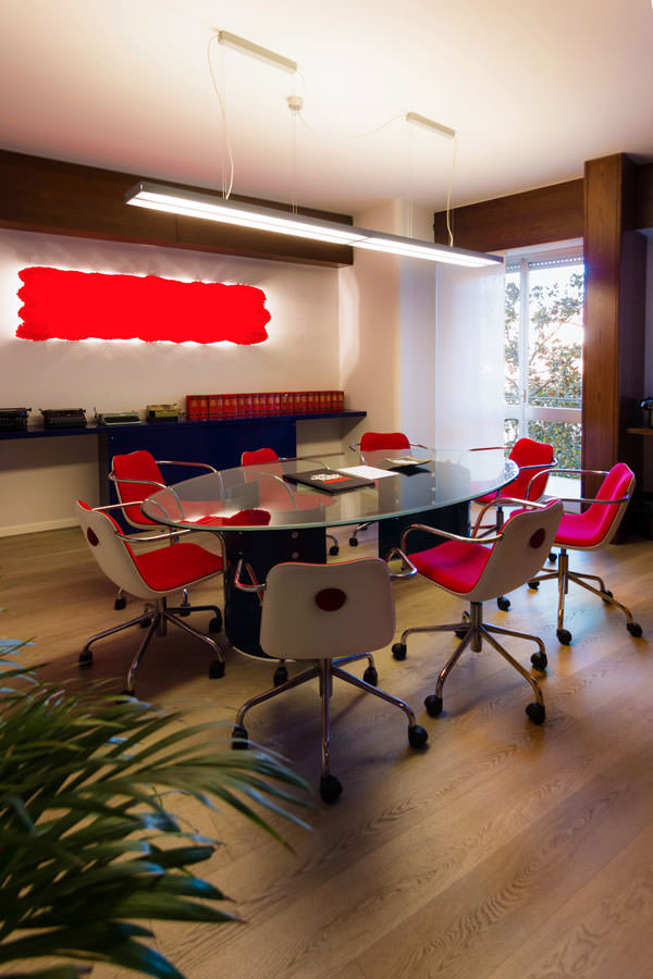 sala-riunioni-tavolo-cristallo sedie lampada parete rosso